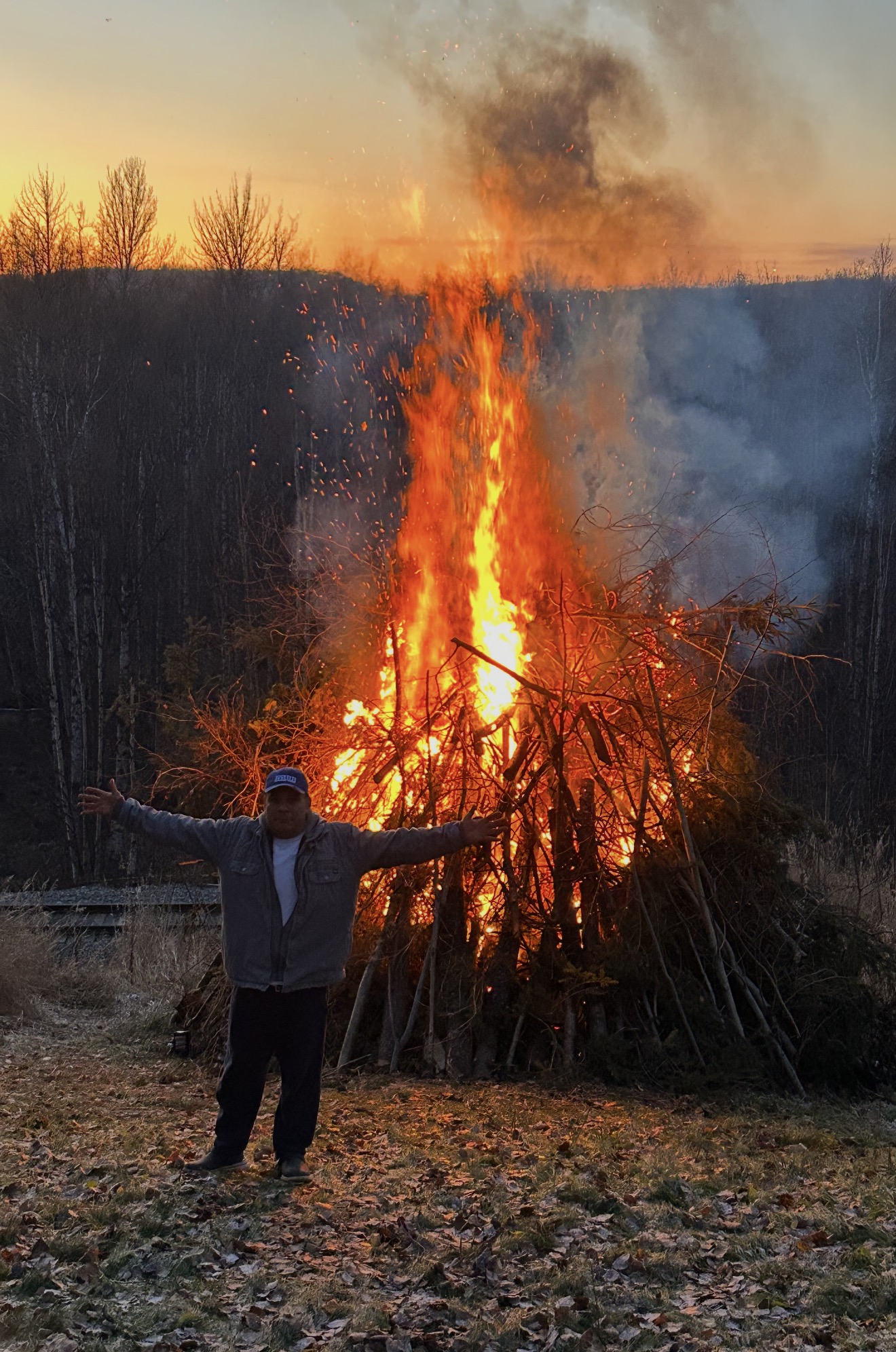 Richard outdoors with his arms spread in front of a large brush fire