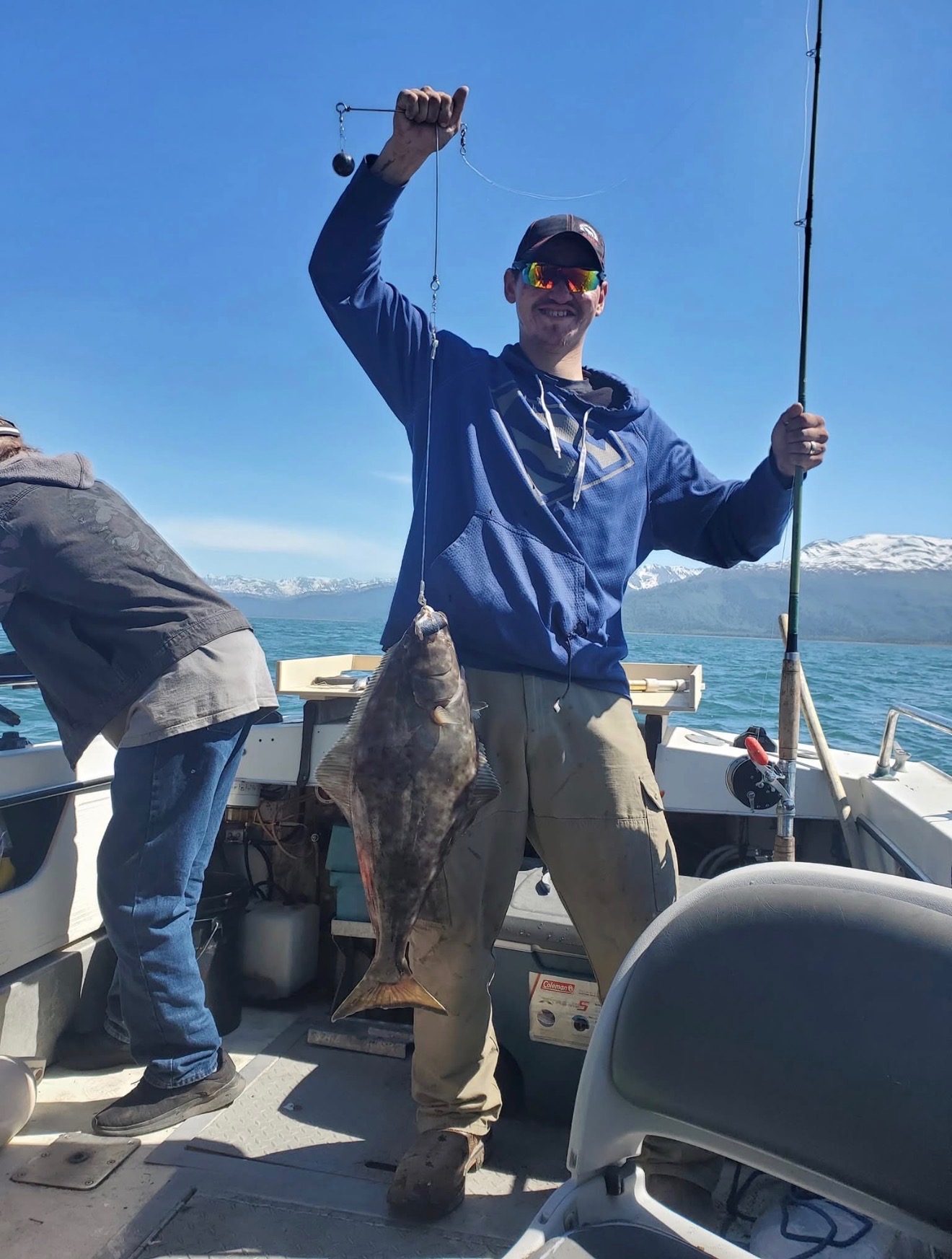 Tom smiling on a fishing boat with his catch and snowy mountains across the water